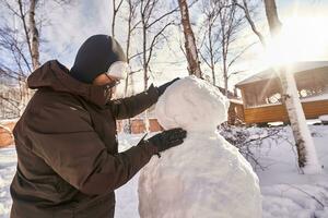 un familia construye un monigote de nieve fuera de blanco nieve en el yarda en invierno. foto