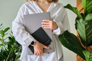 A woman holds a laptop and graphics tablet against a background of greenery. photo