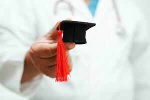 Asian woman doctor holding graduation hat in hospital, Medical education concept. photo