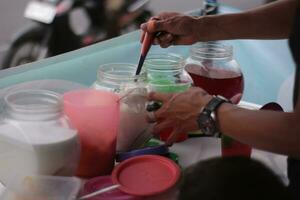 Indonesian street vendor hands prepare a glass of roadside fruit ice as customers patiently wait for their orders. photo