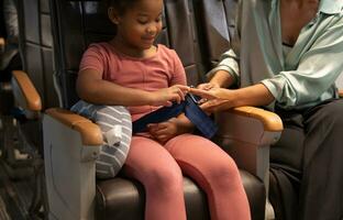 Mother helping daughter for fastening seat belt in airplane cabin photo