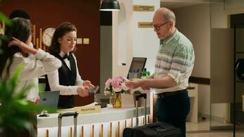 Senior man paying for hotel room with all inclusive services, using card for electronic transaction at pos terminal. Couple in retirement age travelling for leisure, relaxing at five star resort. video