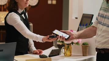 Retired guest using mobile nfc technology to pay for all inclusive room on vacation. Senior man putting smartphone next to pos terminal, electronic payment on retirement trip. Handheld shot. video