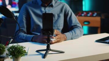 Close up shot of smartphone on holder used by content creator in dimly lit home studio to film video for online streaming platforms. Mobile phone being used by influencer to record footage