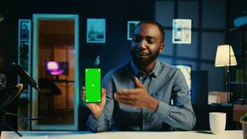 Content creator holding green screen product, being sponsored by tech brand to film unboxing review. BIPOC Influencer showing isolated screen phone recommendation to viewers video