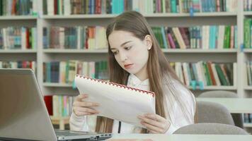 charmant adolescent fille en train de lire cahier de texte à le bibliothèque video