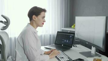 Lovely young woman smiling to the camera while working on her two computers video