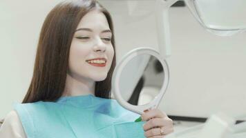 Beautiful woman examining her teeth in the mirror at the dental clinic video