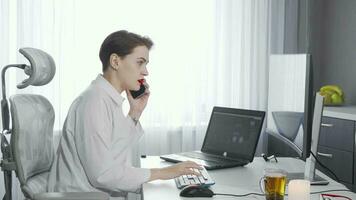 femmina imprenditore parlando su sua Telefono mentre Lavorando su Due computer video