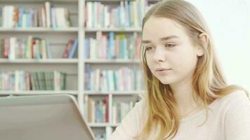 encantador adolescente niña utilizando ordenador portátil a el biblioteca video