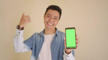 Young Indonesian man with denim style hold smartphone showing green screen.  The footage is suitable to use for man expression and ecommerce content media. video