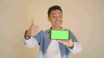 Young Indonesian man with denim style hold smartphone showing green screen.  The footage is suitable to use for man expression and ecommerce content media. video