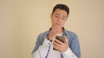 Young Indonesian man with denim style think when check smartphone.  The footage is suitable to use for man expression and lifestyle content media. video