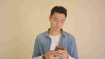 jovem indonésio homem com jeans estilo mensagens de texto em a Smartphone. a cenas é adequado para usar para homem expressão e estilo de vida conteúdo meios de comunicação. video
