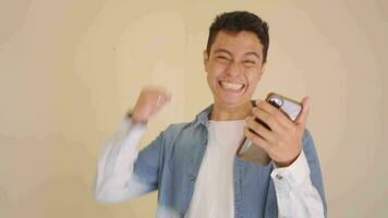 Young Indonesian man with denim style happy when check smartphone.  The footage is suitable to use for man expression and ecommerce content media. video