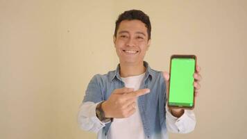 Young Indonesian man with denim style hold smartphone showing green screen.  The footage is suitable to use for man expression and ecommerce content media. video