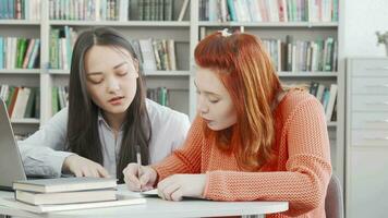 deux femelle élèves travail sur une projet ensemble à le bibliothèque video