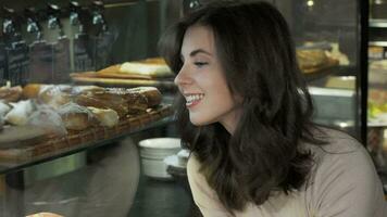 Happy beautiful woman choosing dessert to buy from the bakery display video