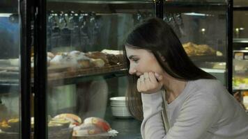 adorável jovem mulher escolhendo sobremesa a partir de a exibição às café fazer compras video