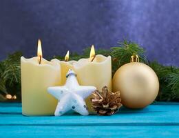 Christmas candles with fire, white sparkling star, golden pine cone and ball on blue wooden background. Behind there are spruce branches. New Year. Copy space photo