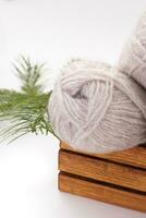 Gray wool skeins or yarn in brown box with spruce branch on white background. Handmade, knitting, hobby. Copy space photo