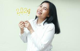 contento asiático compañero de trabajo joven mujer riendo emocionado celebrando 2024 nuevo años por participación oro número velas en mano vistiendo blanco camisa mirando a cámara aislado foto