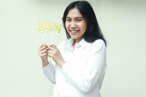 excited asian young woman employee smiling look at camera new years celebration with holding gold candles numbers 2024 wear white formal shirt isolated on white background photo