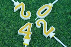 top view of glittering gold candle number 2024 above meadow with green grass, new year eve background concept photo