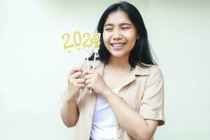 éxito asiático joven mujer sonriente emocionado participación oro velas números 2024 a celebrando nuevo años víspera vestir casual mirando aparte foto