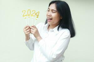 excited young woman asian worker laughing and scream to celebrate 2024 new years eve, looking to gold numeral candles hold on hand wear white shirt isolated photo