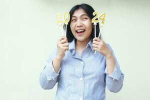 asian young woman excited to celebrating new years eve and thinking new resolution by holding gloden candles numbers 2024 wear blue stripes shirt casual looking away isolated on white background photo