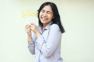 portrait of excited young woman asian coworker laughing full of happiness celebrating 2024 new years eve by holding gold figure candles wear formal grey suit isolated on white background photo