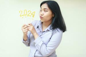 happy young woman asian office coworker celebrating 2024 new years eve and looking to golden figure candle holding on hand with duck face wearing formal grey suit isolated on white background photo