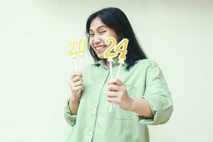 pretty asian young woman excited to celebrating 2024 new years eve by showing gold number candles on her hand wear green shirt isolated on white background photo