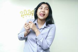 portrait of excited asian young business woman holding golden number candles to celebrate 2024 new years eve wearing grey formal shirt looking aside isolated on white photo