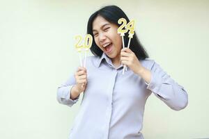 excited beautiful asian young woman coworker shouting to announce exchanging calendar to 2024 new years eve by showing golden candle on her hand wearing formal grey shirt isolated on white background photo