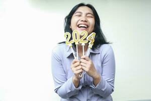 happy asian young woman wear grey formal suit laughing with closed eye and lifting arm hold 2024 figure candle wish for new resolution on new years eve, isolated on white photo