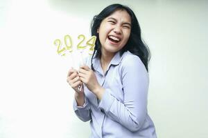 excited asian young business woman laughing and looking away with open mouth while lifting 2024 figure candle hold on hand wearing grey formal suit, isolated, female coworker celebrating new year eve photo