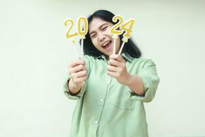 happy asian young woman hipster wearing green over size shirt screaming to camera with raising 2024 number candles holding on hand, isolated over white background photo