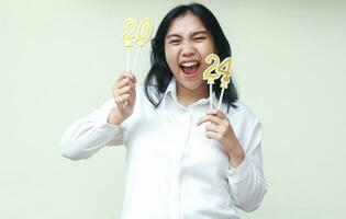 happy asian young business woman screaming and raising arm holding 2024 number candle, isolated, female coworker wearing white formal shirt enjoy new years eve celebration photo
