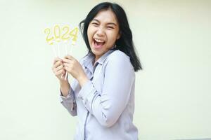 excited young business woman asian screaming with open mouth to camera with raising arm holding 2024 number candle, ecstatic female coworker wearing grey formal suit to celebrating new years eve photo