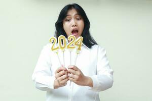 unhappy asian young business woman screaming with open eye looking to 2024 candle number, female coworker wearing formal white shirt, new years eve concept, isolated photo