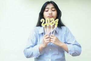 young asian woman wearing blue stripes casual shirt thinking and imagine while looking down to 2024 figure candle holding on hand, new years eve concept, isolated on white photo