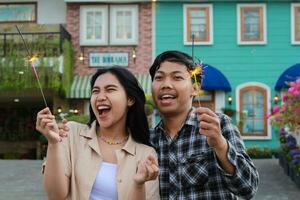 exited asian young couple holding sparkler and shouting in the yard of vintage wooden house celebrating new years eve wear stylish outer and flannel, look away photo