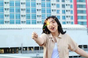 happy asian young woman holding sparklers celebrate new year eve in outdoor roof top with city building background photo