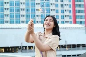 beautiful asian young woman holding sparklers firework and laughing in new year eve celebration standing in roof top outdoor with urban building background photo