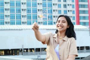 beautiful asian young woman holding sparklers firework and laughing in new year eve celebration standing in roof top outdoor with urban building background photo