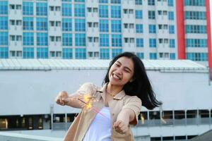 happy asian young woman hipster holding sparklers firework celebrate new year eve with dancing in roof top apartment with urban building background photo