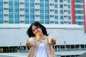 happy asian young woman hipster holding sparklers firework celebrate new year eve with dancing in roof top apartment with urban building background photo