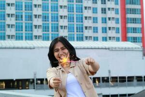 happy asian young woman hipster holding sparklers firework celebrate new year eve with dancing in roof top apartment with urban building background photo